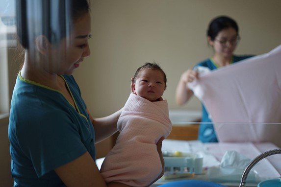 Medical professional holding an infant wrapped in a light pink blanket