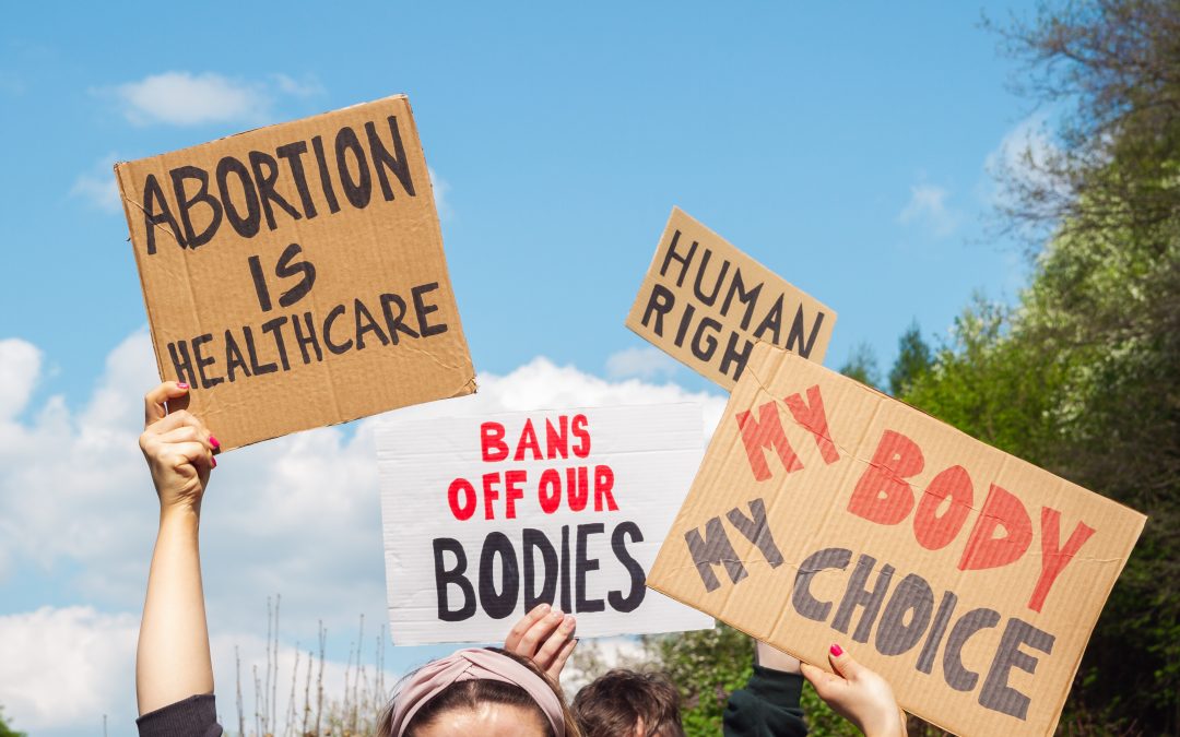 Protestors' signs that read ABORTION IS HEALTHCARE, BANS OFF OUR BODIES, HUMAN RIGHT, and MY BODY MY CHOICE
