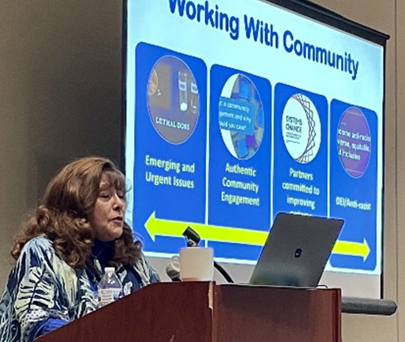 Stephanie Salazar-Rodriguez speaking at a podium with a presentation behind her that says "Working with Community"